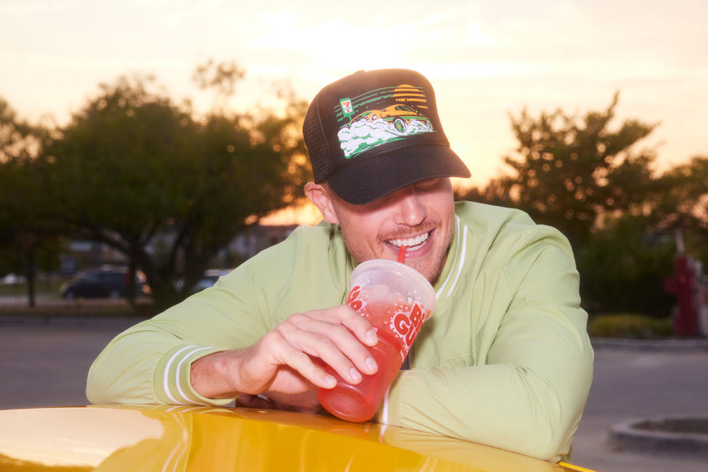 Man drinking a Big Gulp while wearing a Cars of 7-Eleven hat.